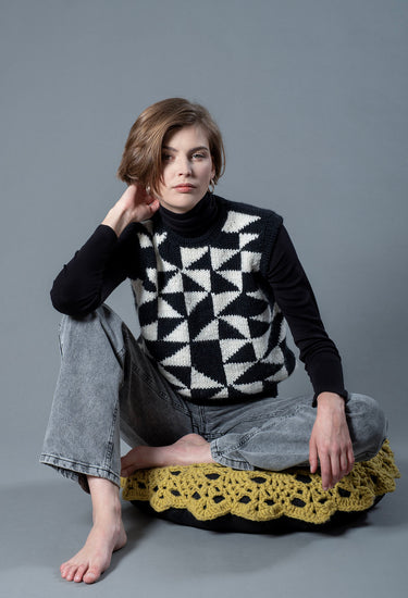Sitting woman wearing a wool vest. The vest has black and white triangular patterns on the front.